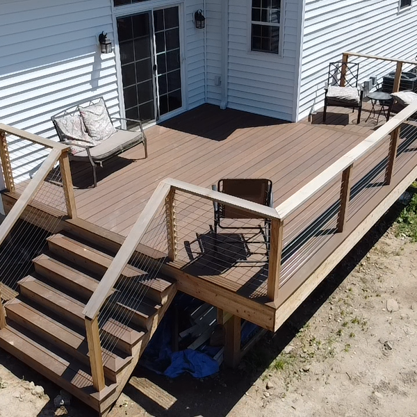 A custom deck off the back of the house with patio chairs sitting on it. The deck is finished with a cable railing system.