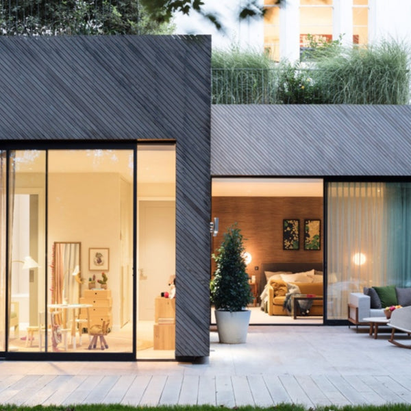 A simplistic house completed with dark grey Kebony the patio out the one door has a outdoor couch and chair. 