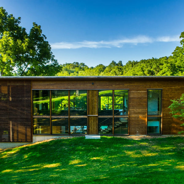 A house in the woods with Kebony siding. The house has large open windows and a outdoor frame. 