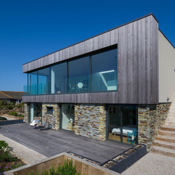 A large modernized house completed with Kebony siding at the top and brick at the bottom. There is an outdoor patio and stairs build outside of the house. 