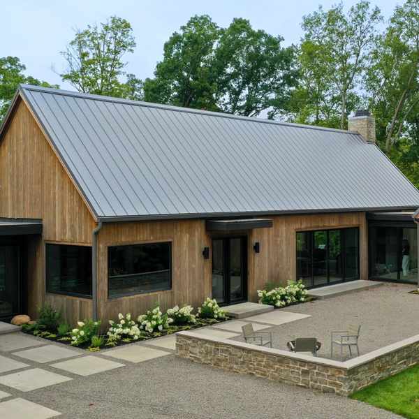 A house in the woods completed with Kebony siding and finished with landscaping. There is a few chairs in the front area of the house.