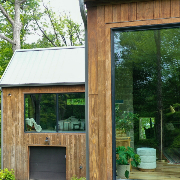 A house with Kebony siding peering into the windows where a chair is visible as well as the garage. 