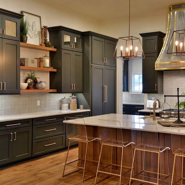 Clean kitchen with black Kith One Cabinetry with clear stools and new appliances. Also has a overhead oven fan and a plant on the island. 