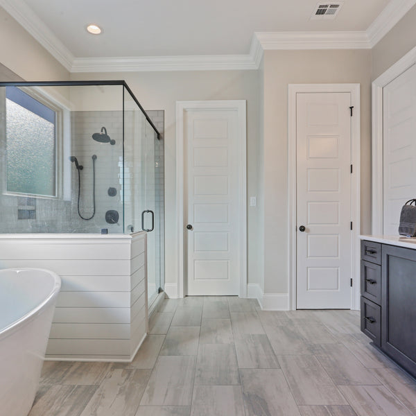 A minimalistic bathroom with a glass shower and stand alone tub. Completed with black Kith One Cabinetry and white doors and accents.