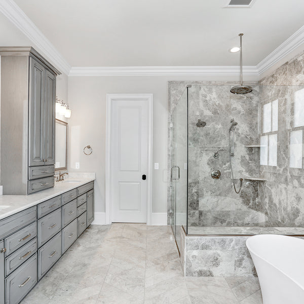 A very open bathroom with a glass shower and stand alone tub. Grey Kith One Cabinetry and white marble countertops with. 