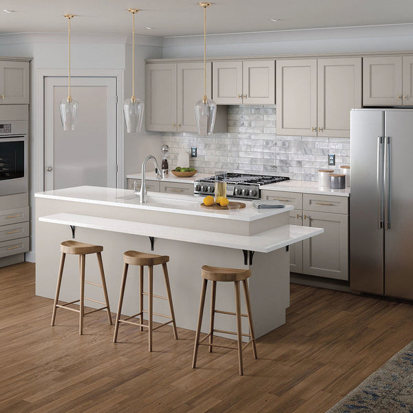 Off white Mantra cabinets in a kitchen setting. The island in the center has brown stools under it and grey appliances. 