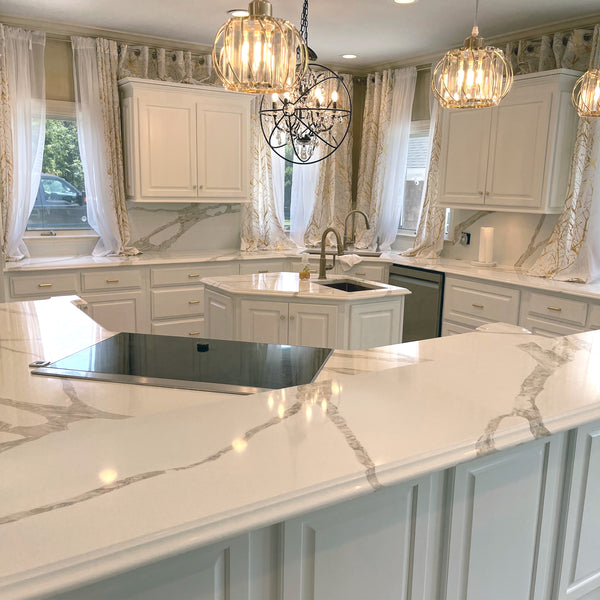 A kitchen space completed with Vicostone Quartz countertops and round light fixtures. There are curtains draped in the windows and stainless steel appliances. 