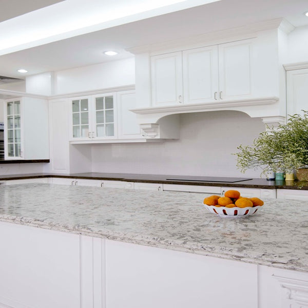 A white simplistic kitchen with marble Vicostone Quartz countertops and white cabinets. Fruit and flowers are used as decor on the island.