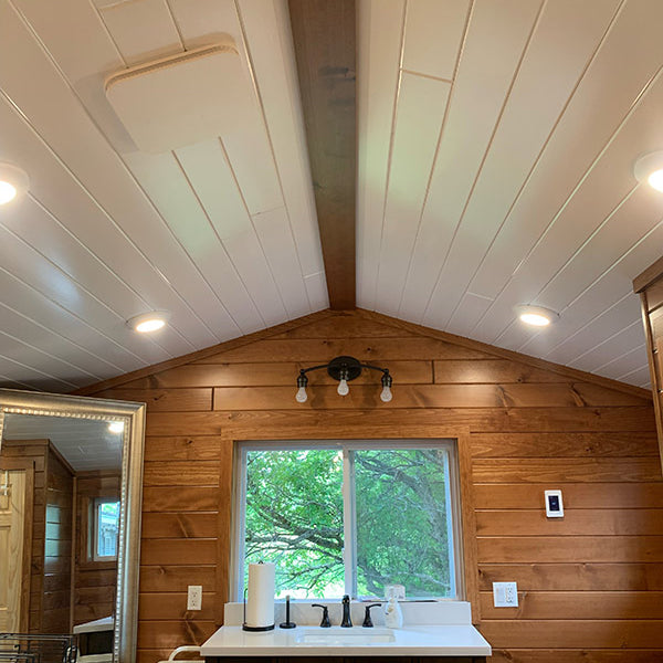 A bathroom with cathedral ceiling finished with a white pine tongue and grove ceiling.  Bathroom has a vanity with a white countertop and brown cabinetry. 