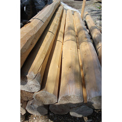 A stack of not drilled, beige-colored wooden posts, likely made from cedar, displayed outdoors.